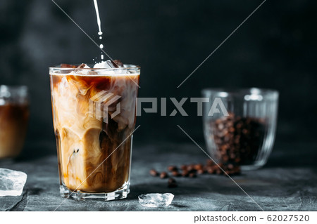 Milk Being Poured Into Iced Coffee on a dark table 62027520
