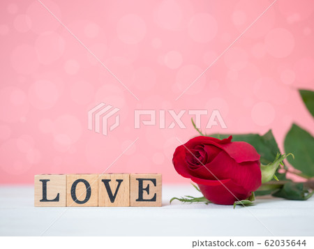 Close up at red rose flower with LOVE wooden cube on wooden slate and pink background. Use for valentines day, love and relationship concept. Close up at red rose flower with LOVE wooden cube on wooden slate and pink background. Use for valentines day, love and relationship concept. 62035644