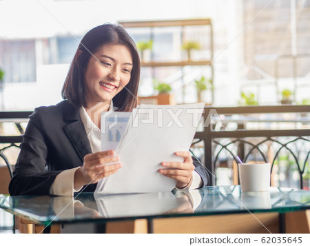 Happy Asian business woman sitting and looking document in cafeteria. Adorable Asian business woman smiling while success in job at cafeteria. Happy Asian business woman sitting and looking document in cafeteria. Adorable Asian business woman smiling while success in job at cafeteria. 62035645