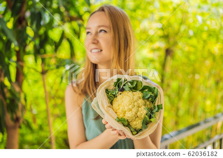 Cauliflower in a reusable bag in the hands of a young woman. Zero waste concept Cauliflower in a reusable bag in the hands of a young woman. Zero waste concept 62036182