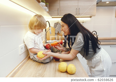 Mother with little son eating fruits in a kitchen Mother with little son eating fruits in a kitchen 62038626