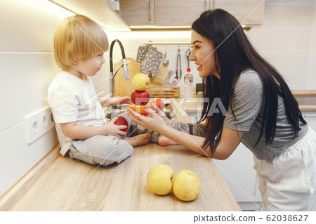 Mother with little son eating fruits in a kitchen Mother with little son eating fruits in a kitchen 62038627