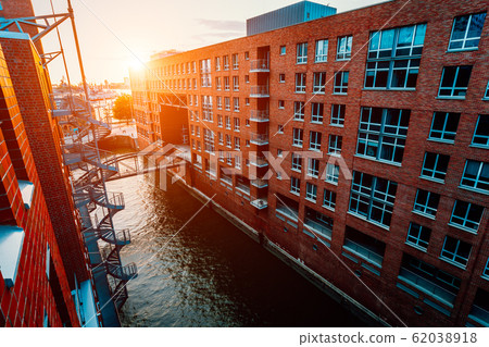 HafenCity canal. Circular staircase, bridge over canal and red brick buildings in the old warehouse district Speicherstadt in Hamburg in golden hour sunset light, Germany. View from above HafenCity canal. Circular staircase, bridge over canal and red brick buildings in the old warehouse district Speicherstadt in Hamburg in golden hour sunset light, Germany. View from above 62038918