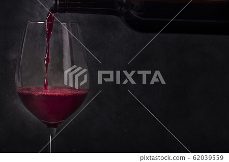 Pouring wine into a glass from a bottle, side view on a black background with a place for text 62039559