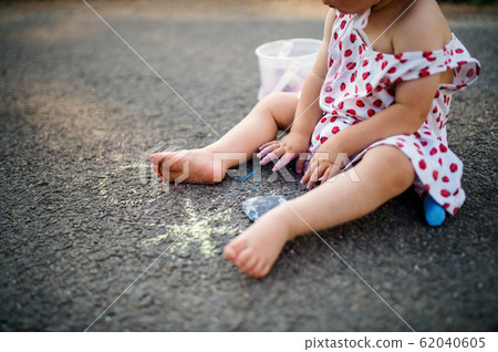 Unrecognizable toddler girl outdoors in countryside, chalk drawing on road. 62040605