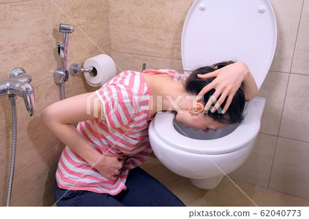 Young sick woman with pain in stomach is vomiting in toilet sitting on the floor at home, flu symptom. Young sick woman with pain in stomach is vomiting in toilet sitting on the floor at home, flu symptom. 62040773