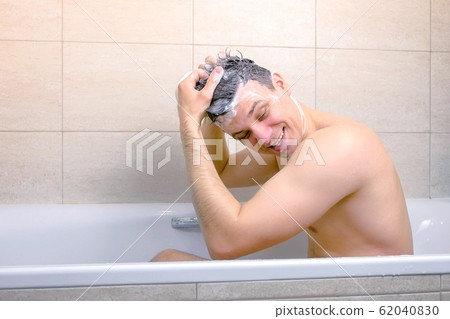 Man is washing his head with shampoo and making a Mohawk from hairs sitting in bathtub. 62040830