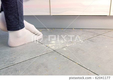 Woman on the dirty floor in the kitchen. Leftovers and crumbs on the kitchen floor. Legs close-up. Woman on the dirty floor in the kitchen. Leftovers and crumbs on the kitchen floor. Legs close-up. 62041177