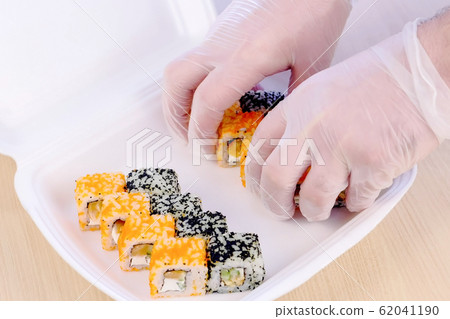Cook puts rolls on plastic box with wasabi and ginger for delivery in restaurant. Hands close-up. 62041190
