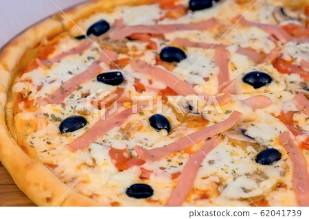 Pizza with ham and cheese on wooden board on the table. Close-up view. Side view. 62041739