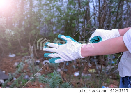 Volunteer woman putting on gloves to pick trash on forest, hands closeup. Volunteer woman putting on gloves to pick trash on forest, hands closeup. 62045715