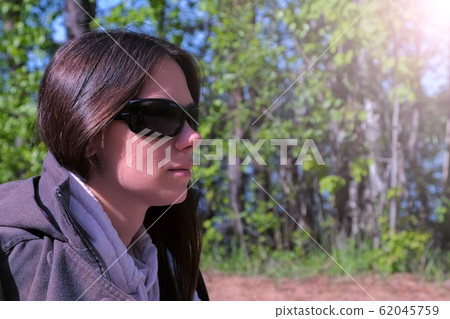 Portrait of woman in sunglasses sitting resting in forest on riverbank. 62045759