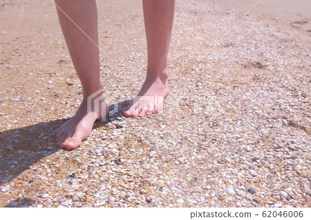 Barefooted woman walks on sea shells on sand beach makes nature feet massage. 62046006
