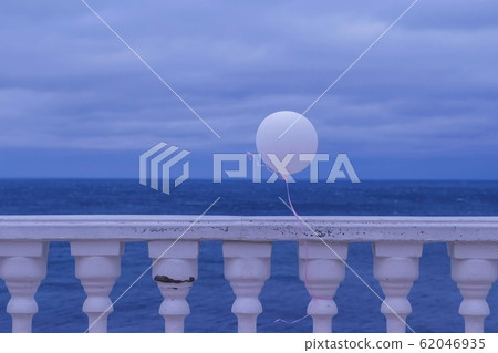 White balloon in the wind tied to the fence on sea waterfront in a cloudy day. White balloon in the wind tied to the fence on sea waterfront in a cloudy day. 62046935