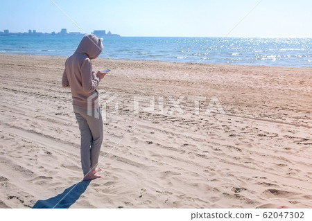 Unrecognizable woman is typing on phone on the beach by sea. Unrecognizable woman is typing on phone on the beach by sea. 62047302