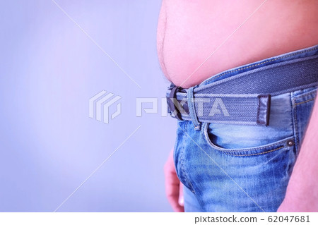 Man's fat stomach is hanging out of jeans, side view. Man's fat stomach is hanging out of jeans, side view. 62047681
