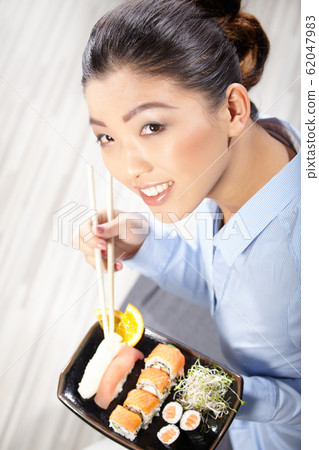 Beautiful young woman eating sushi. Shallow depth Beautiful young woman eating sushi. Shallow depth 62047983