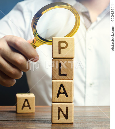 Wooden blocks with the word Plan and magnifying glass in the hands of a businessman. Strategy planning. Management business concept. Improving the efficiency of the company's sales. Financial target 62048444