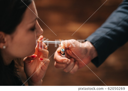 A gentleman lights a cigarette of a beautiful woman. 62050269