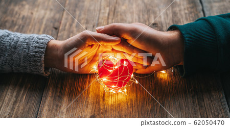Two hands holding a red heart shape covered with led lights on wooden and bokeh lights background. Valentines day and romance concept. 62050470