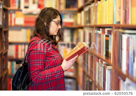 Intellectual Teenage girl choose books and pick them from a library or bookstore. Intellectual Teenage girl choose books and pick them from a library or bookstore. 62050576