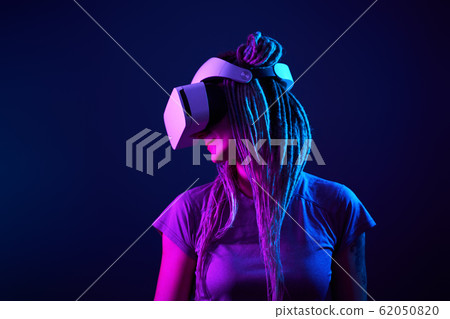 Woman is using virtual reality headset. Neon light studio portrait. 62050820