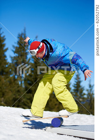 Male snowboarder balancing on snowboard in white snow on background of blue sky and spruce trees. Male snowboarder balancing on snowboard in white snow on background of blue sky and spruce trees. 62052792