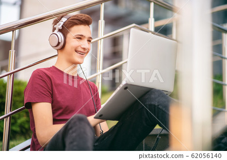 Smiling teenage boy with a laptop on the street. Smiling teenage boy with a laptop on the street. 62056140