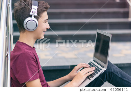 Smiling teenage boy with a laptop on the street. Smiling teenage boy with a laptop on the street. 62056141