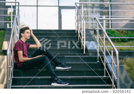 Dreaming guy in earphones holds a mobile phone in Dreaming guy in earphones holds a mobile phone in 62056142
