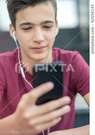 Teenage boy is using mobile phone, outdoors. Teenage boy is using mobile phone, outdoors. 62056143