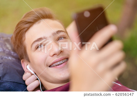 Happy teenage boy is using mobile phone, outdoors. Happy teenage boy is using mobile phone, outdoors. 62056147