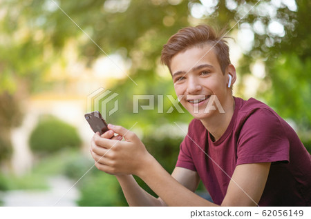 Happy teenage boy is using mobile phone, outdoors. Happy teenage boy is using mobile phone, outdoors. 62056149