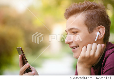 Happy teenage boy is using mobile phone, outdoors. 62056151