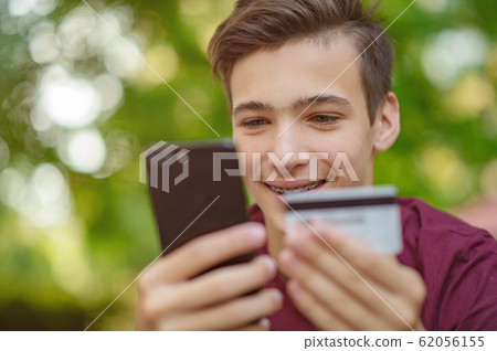 Teenage boy with a credit card and phone makes Teenage boy with a credit card and phone makes 62056155