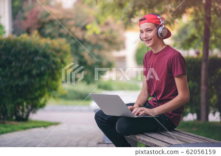 Smiling teenage boy with a laptop in the park. Smiling teenage boy with a laptop in the park. 62056159