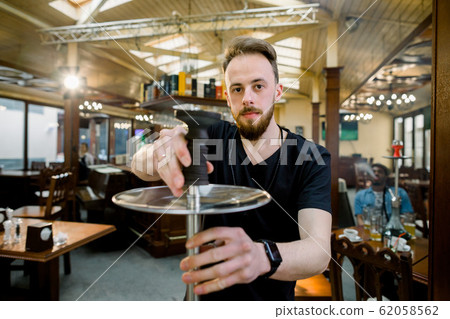 Hookah Server Waiter Prepares A Shisha Pipe For Smoking Hookah Server Waiter Prepares A Shisha Pipe For Smoking 62058562
