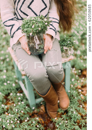 beautiful girl with long hair sitting on the chair and holding glass jar with flowers while walking through the green forest beautiful girl with long hair sitting on the chair and holding glass jar with flowers while walking through the green forest 62058685