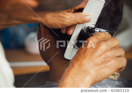 Closeup hand of hairdresser cutting hair with clipper at local barber shop. 62065319