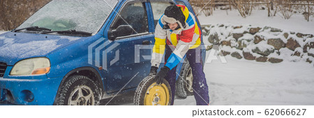 Winter accident on the road. A man changes a wheel during a snowfall. Winter problems BANNER, LONG 62066627