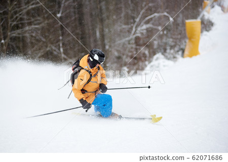 Young man skier in ski sportswear doing skillful maneuvers on skis. Skiing and turning on snow-covered mountain descent Young man skier in ski sportswear doing skillful maneuvers on skis. Skiing and turning on snow-covered mountain descent 62071686