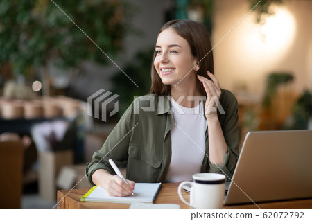 Joyful girl looking to the side holding pen over a notebook. Joyful girl looking to the side holding pen over a notebook. 62072792