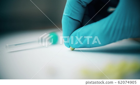 Hand in sterile medical glove puts small pill on the desk 62074905