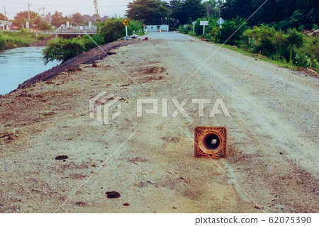 The old traffic cone falling on the road that was being repaired along the irrigation canal for agriculture. The old traffic cone falling on the road that was being repaired along the irrigation canal for agriculture. 62075390