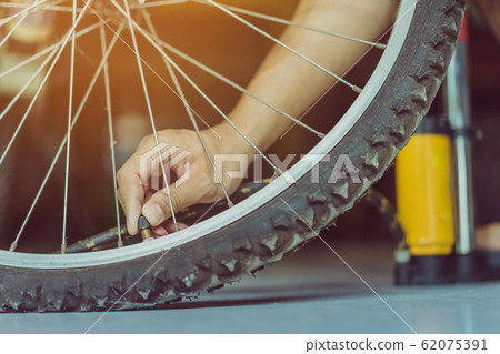 Close-up of a young man prepare to pumping the old bicycle wheel in his home. . Close-up of a young man prepare to pumping the old bicycle wheel in his home. . 62075391