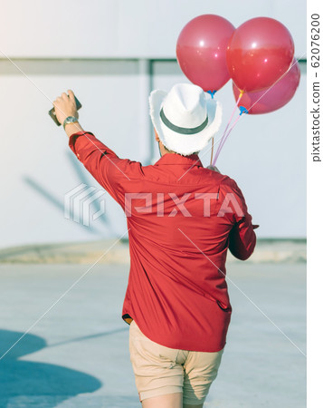 Back view of gay man in red shirt holding red balloons from the car park to join the party in the afternoon. 62076200