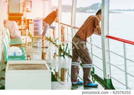 Asian man stands on baluster of ferry for relaxing and look at the ocean and island. Asian man stands on baluster of ferry for relaxing and look at the ocean and island. 62076202