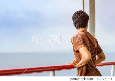 Asian man stands on baluster of ferry for relaxing and look at the ocean and island. 62076203