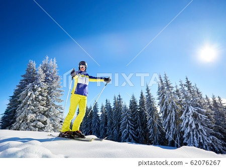 Happy woman posing on skis before skiing. Sunny day at ski resort. Clear blue sky, snow-covered fir trees on background. Happy woman posing on skis before skiing. Sunny day at ski resort. Clear blue sky, snow-covered fir trees on background. 62076267