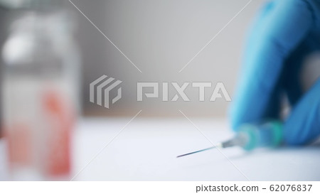 Hand in sterile medical glove puts syringe on the desk 62076837